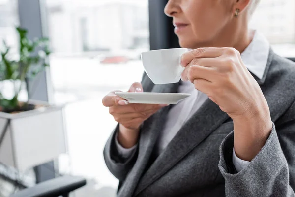 Vista ritagliata di economista che tiene tazza di caffè e piattino in ufficio — Foto stock