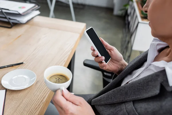 Vista parcial del economista sentado en el escritorio con taza de café y teléfono inteligente - foto de stock