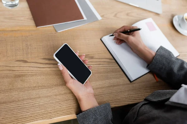 Partial view of economist with smartphone writing in notebook near folders — Foto stock