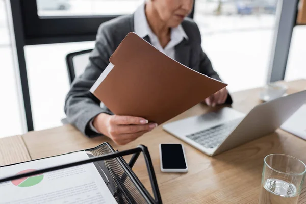 Vista recortada de la carpeta de retención economista mientras trabaja cerca de la computadora portátil - foto de stock