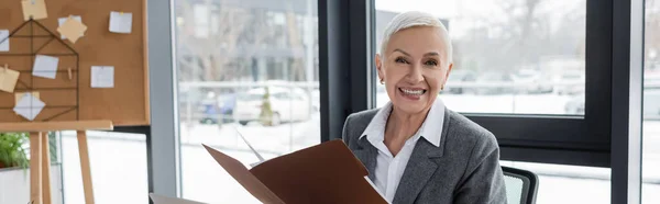 Smiling banker with folder looking at camera near blurred corkboard on background, banner — Photo de stock