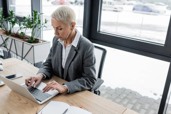 Economista elegante con capelli grigi corti che scrivono su computer portatile in ufficio — Foto stock