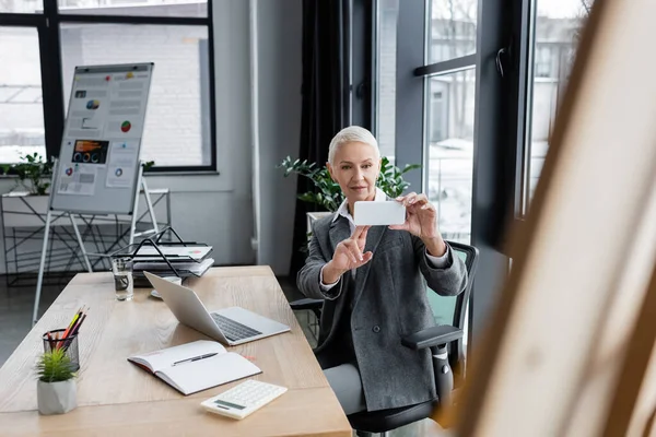 Economist taking photo of blurred flip chart near laptop, blank notebook and calculator — Fotografia de Stock