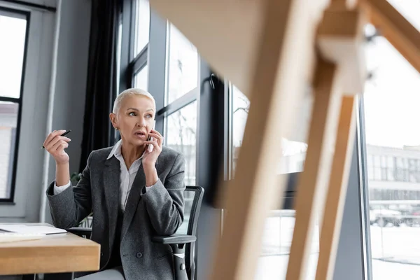 Anziano finanziere parlando su smartphone mentre seduto alla scrivania in primo piano sfocato — Foto stock