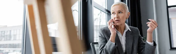 Banker holding pen while talking on mobile phone on blurred background, banner — Stock Photo