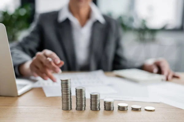 Enfoque selectivo de monedas de plata apiladas cerca de banquero recortado sentado sobre fondo borroso - foto de stock