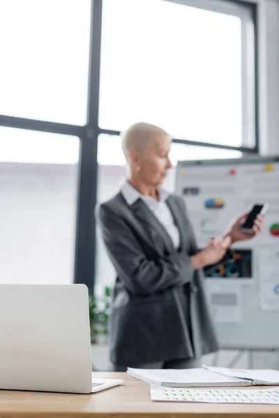 Blurred banker standing near flip chart with graphs during video call on smartphone - foto de stock