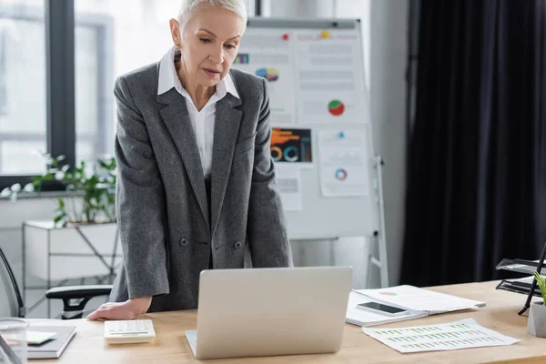 Economista con videoconferenza su laptop vicino a flip chart su sfondo sfocato — Foto stock