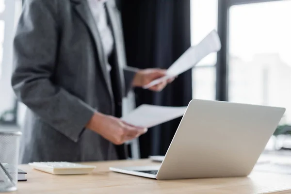 Selective focus of laptop near cropped banker with papers on blurred background — стоковое фото