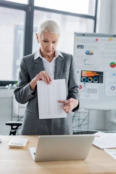 Banker pointing at document during video chat on laptop near blurred flip chart with analytics — Photo de stock