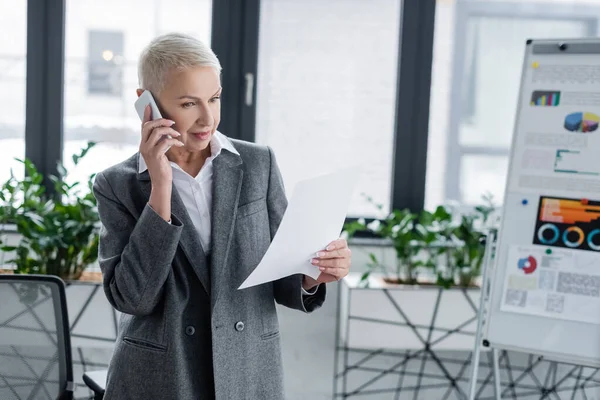 Banker schaut auf Dokument, während er auf dem Smartphone spricht, fast verschwommenes Flipchart — Stockfoto