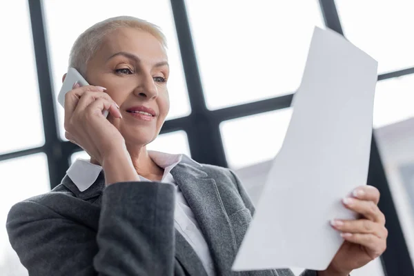 Low angle view of smiling financier with white paper talking on mobile phone — Stock Photo
