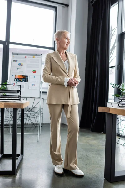 Full length view of elegant and smiling banker standing near flip chart on background — Stock Photo