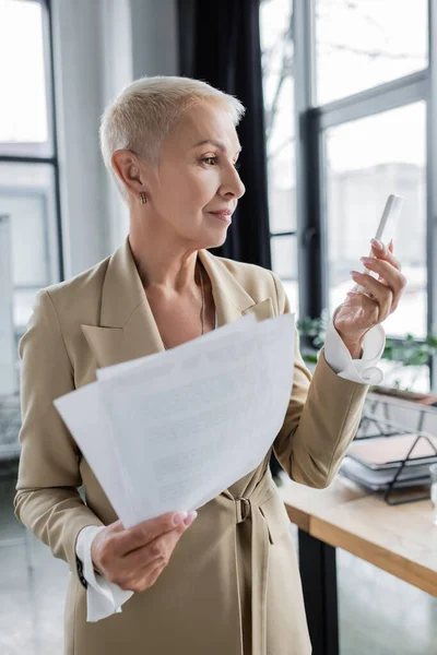 Économiste principal avec des documents regardant le téléphone portable dans le bureau — Photo de stock