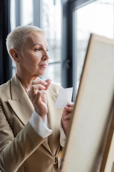 Senior economist with short hair holding paper note near blurred flip chart - foto de stock