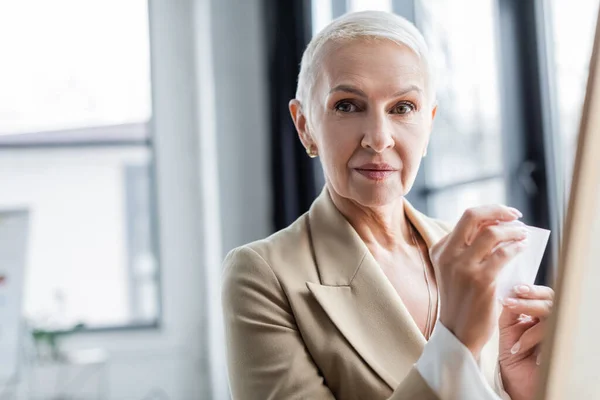 Stylish banker with paper note looking at camera in office — Stock Photo