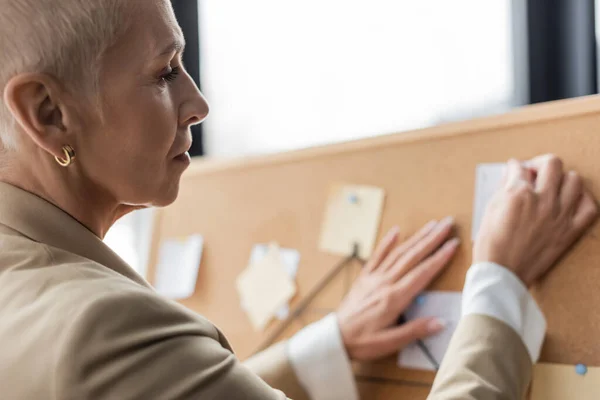 Senior economist applying paper notes on corkboard in office — Stock Photo