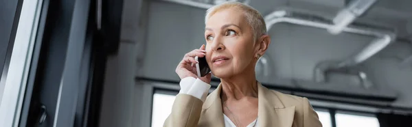 Economista senior llamando al teléfono móvil y mirando hacia otro lado en la oficina, pancarta - foto de stock