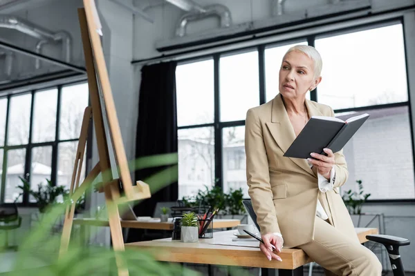 Banker with notebook and pen sitting on desk and looking at flip chart — стоковое фото