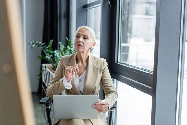 Thoughtful economist in formal wear sitting with laptop in office — Stock Photo