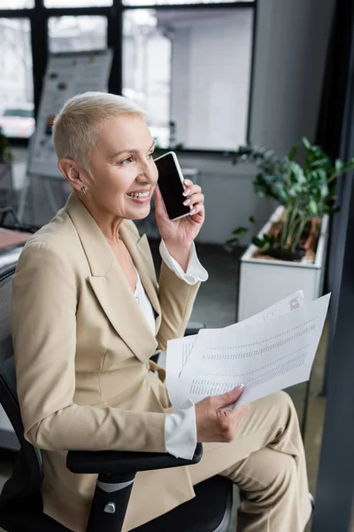 Cheerful banker sitting in office with documents and listening voice message — Stock Photo