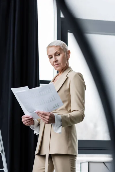 Serious economist in formal wear looking at papers in office — Stock Photo