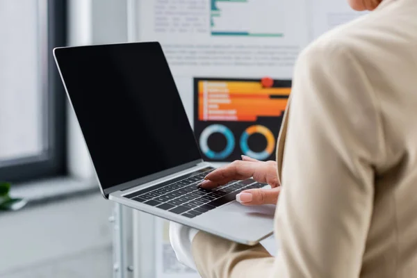 Cropped view of banker using laptop with blank screen near blurred flip chart with graphs — Stockfoto