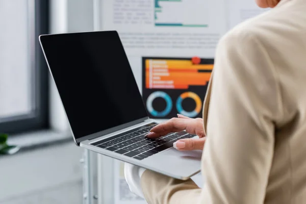 Cropped view of banker using laptop with blank screen near blurred flip chart with graphs — Foto stock