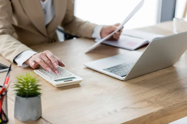 Partial view of accountant with documents using calculator near laptop — Stock Photo