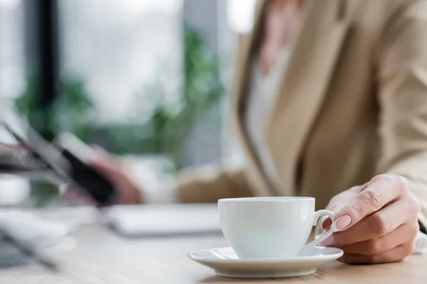 Selective focus of white coffee cup near cropped banker on blurred background — Stock Photo