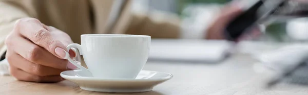 Partial view of blurred economist near white coffee cup and saucer, banner — Stock Photo