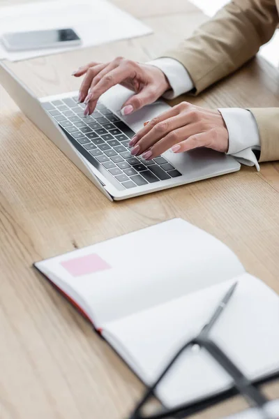 Teilansicht des Finanziers beim Tippen auf Laptop neben leerem Notizbuch auf unscharfem Vordergrund — Stockfoto