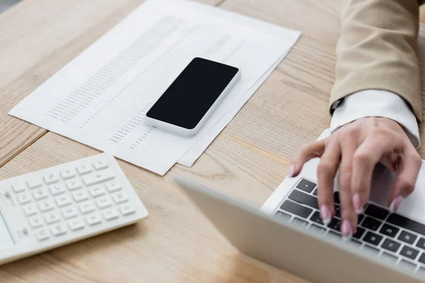 Cropped view of accountant typing on laptop near smartphone, calculator and documents — Stock Photo