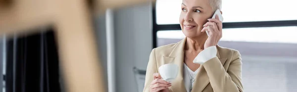 Happy economist with coffee cup talking on mobile phone on blurred foreground, banner — Foto stock