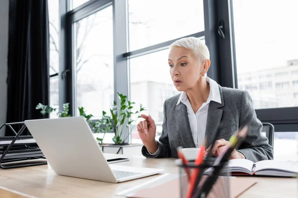 Überraschte Geschäftsfrau zeigt bei Videokonferenz im Büro auf Laptop — Stockfoto