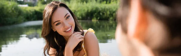 Cheerful woman flirting and looking at blurred boyfriend, banner — Stock Photo