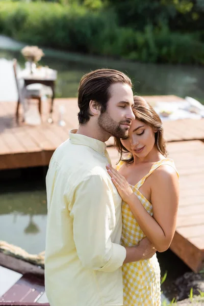 Felice giovane donna che abbraccia con uomo barbuto vicino al lago — Foto stock