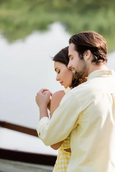 Vue latérale de barbu homme étreignant petite amie sensuelle près du lac — Photo de stock