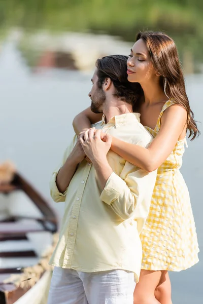 Mujer joven en vestido abrazando novio barbudo cerca del lago - foto de stock