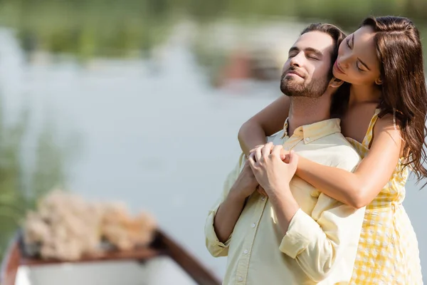 Молода жінка з закритими очима обіймає бородатого хлопця біля озера — стокове фото