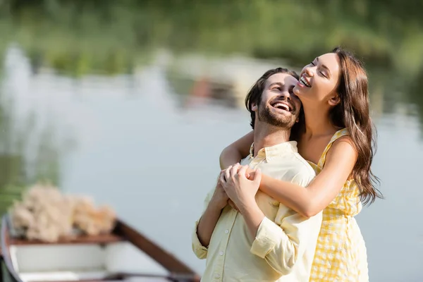 Jeune femme en robe câlin heureux copain barbu près du lac — Photo de stock