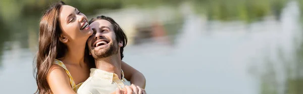 Joven mujer abrazando feliz barbudo novio cerca del lago, bandera - foto de stock