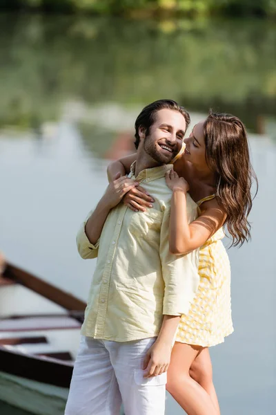 Feliz jovem mulher no vestido abraçando namorado barbudo perto do lago — Fotografia de Stock