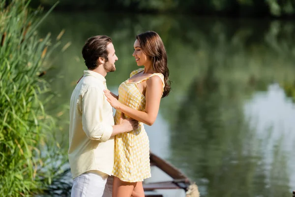 Feliz jovem casal olhando uns para os outros perto do lago — Fotografia de Stock