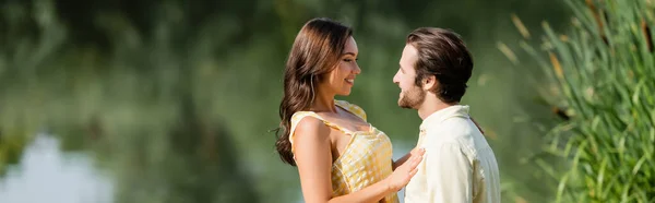 Feliz joven pareja mirándose el uno al otro cerca del lago, bandera - foto de stock