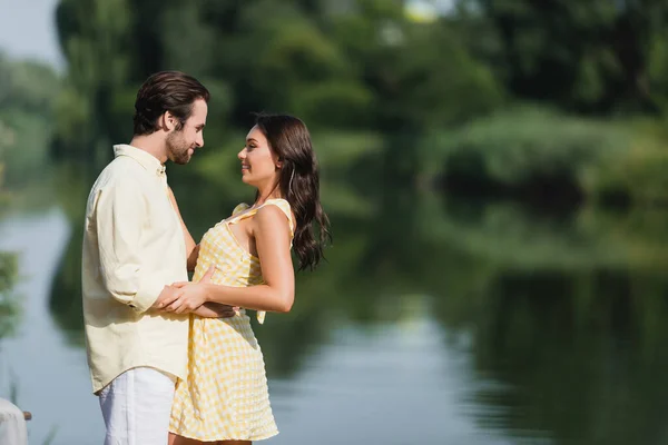 Vue latérale du jeune couple heureux se regardant près du lac — Photo de stock