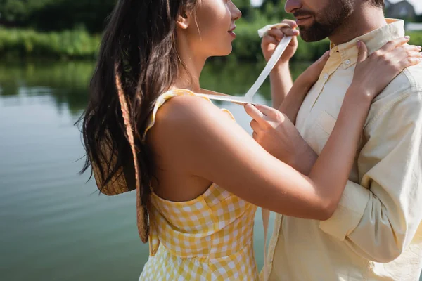 Cropped view of bearded man tying ribbon on straw hat of woman — Stock Photo