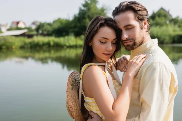 Tender couple with closed eyes hugging near lake — Stock Photo