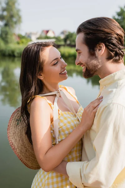 Junge Frau mit Strohhut umarmt fröhlichen Freund in der Nähe des Sees — Stockfoto