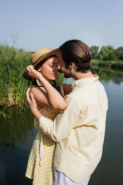 Feliz jovem casal em roupas de verão abraçando perto do lago — Fotografia de Stock